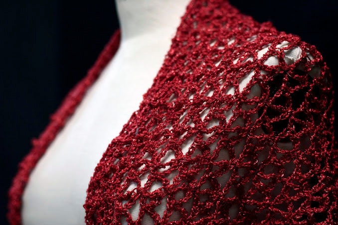 Close-up of the red lurex crochet shawl on a mannequin's shoulder, showing the openwork stitch pattern.